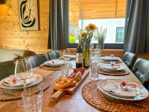 Una mesa de comedor dispuesta con platos, vasos y una botella de vino, rodeada de sillones de cuero.