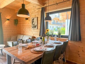 A wooden interior with a dining table set for six, a sofa, and a window with a view of buildings. - Lovely holiday home on park near ski resort (Rattendorf)