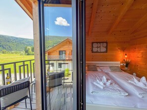 Une cabane en bois avec un balcon, un lit aux oreillers soigneusement disposés et une œuvre d’art encadrée accrochée au mur.