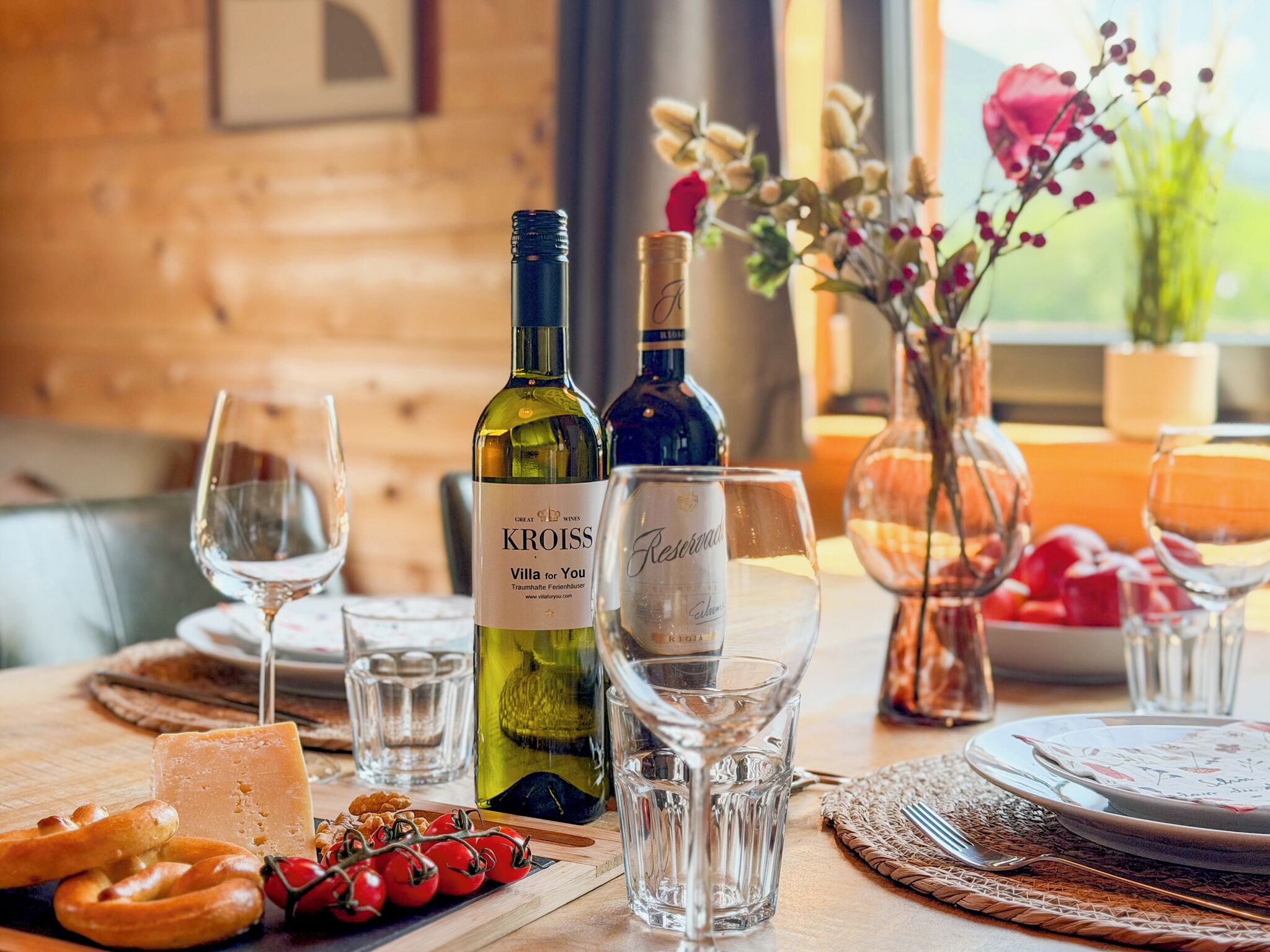 A table set with wine glasses, a bottle of Kroiss wine, cheese, pretzels, and tomatoes.