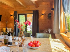 Un intérieur en bois avec une table à manger, des bouteilles de vin, un vase rempli de fleurs et un saladier de fruits.