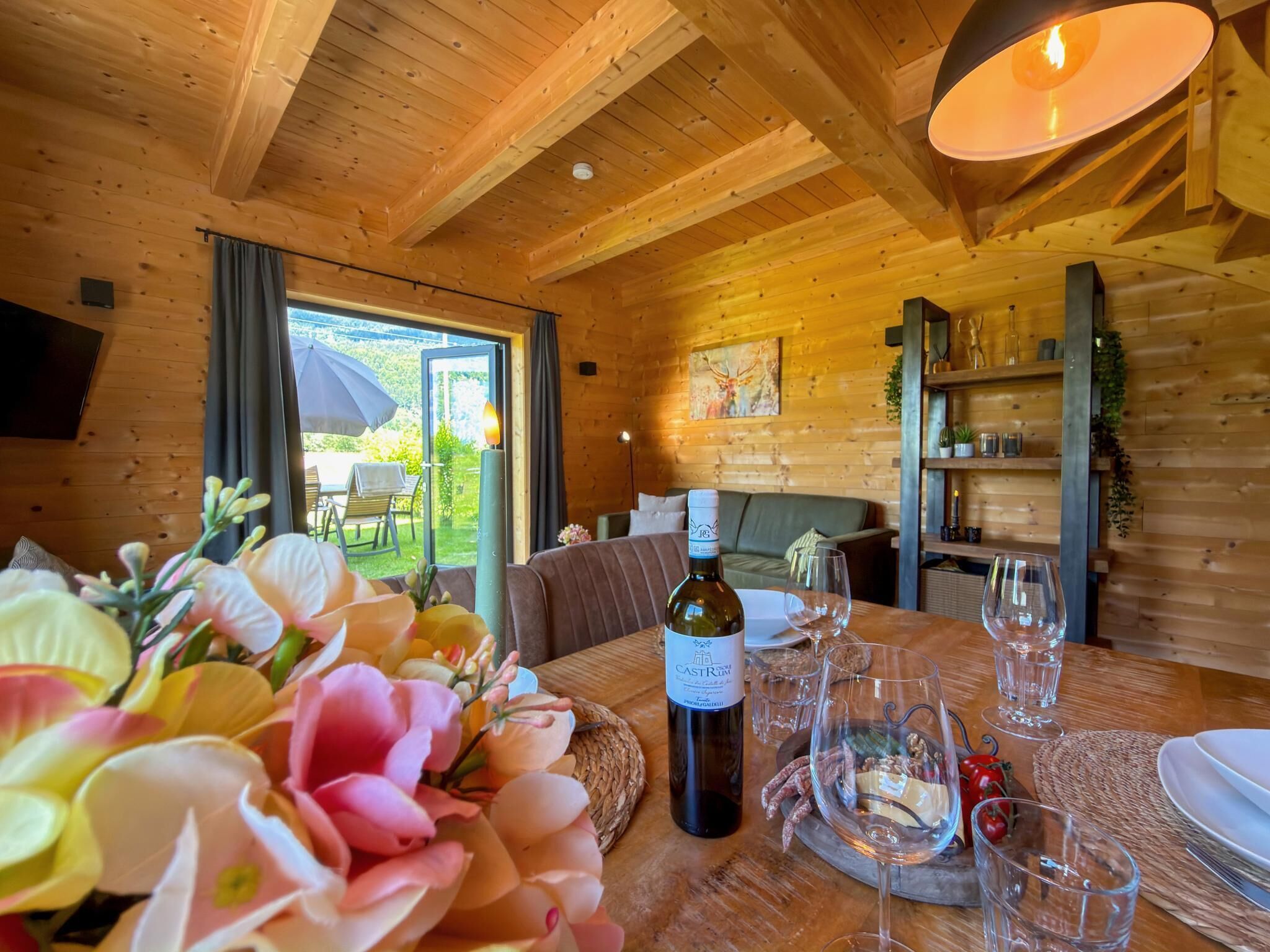 A wooden interior with a dining table set for two, a bottle of Castrolu wine, and a view of the outdoors.