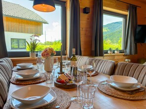 Ein Esstisch ist gedeckt mit Tellern, Gläsern und einer Flasche, mit Blick auf Grünflächen und ein Haus im Hintergrund.