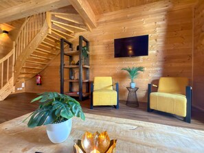 A wooden interior with a staircase, two yellow chairs, a potted plant, a shelf with decorative items, and a flat-screen TV mounted on the wall. - Lovely holiday home on park near ski resort (Rattendorf)