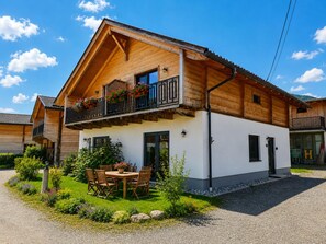 Eine Holzhütte mit einem Balkon, einem Essbereich mit Sitzgelegenheiten im Freien und einer Schotterauffahrt.