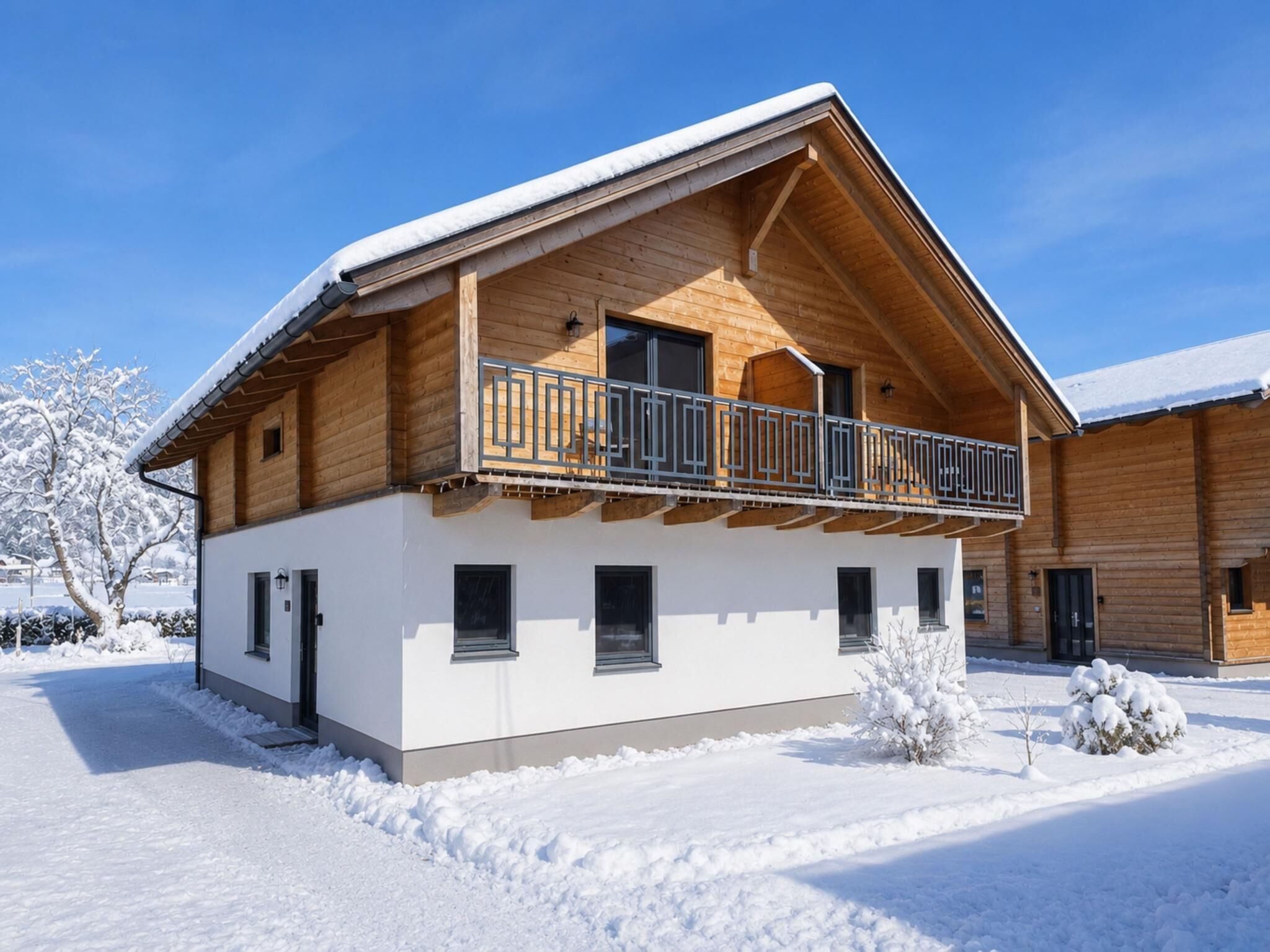 En toetages træchalet med balkon, sneklædte omgivelser og en klar himmel.