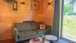 A wooden interior with a sofa, two round tables, and wall-mounted lighting. - Lovely holiday home on park near ski resort (Rattendorf)