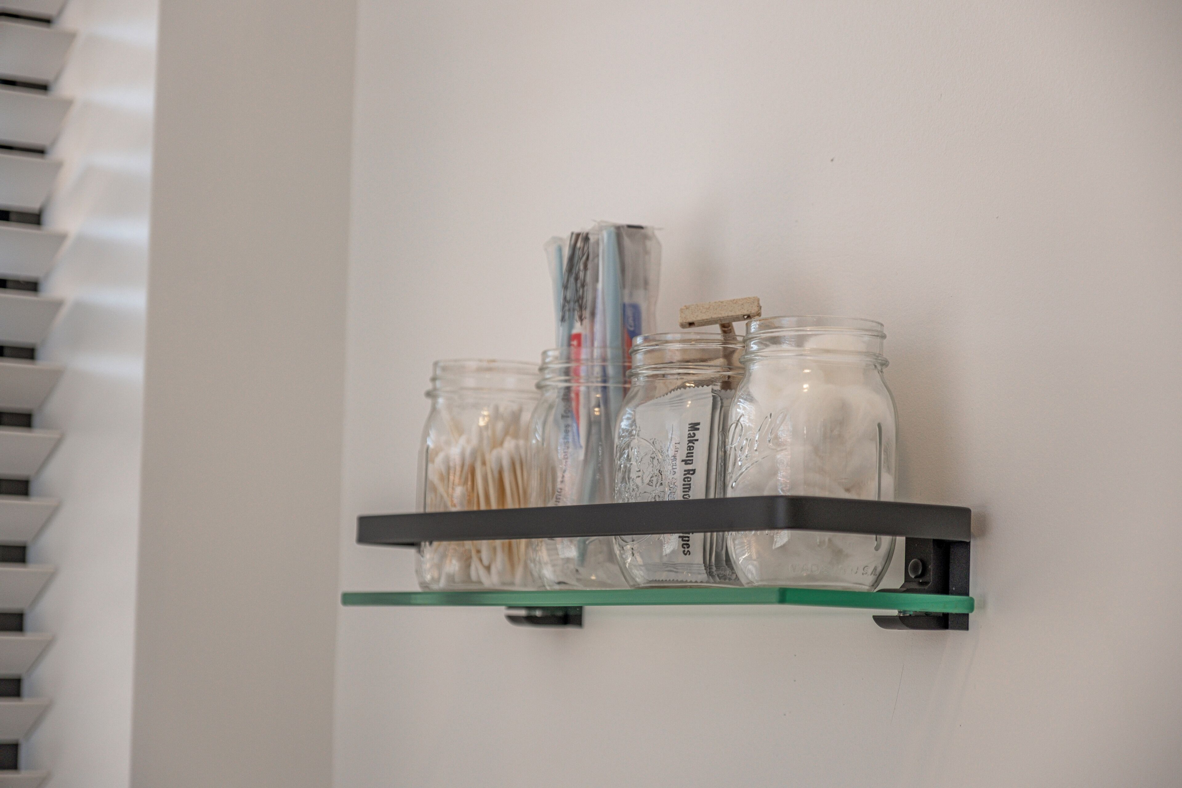 A glass shelf with jars containing various items.
