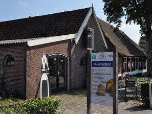 A brick building with a traditional thatched roof, a signboard with text, and a statue of a woman.