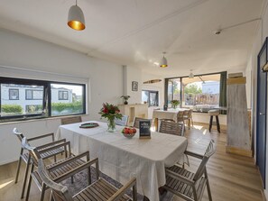 A dining area with a table set for four, surrounded by wooden chairs, with a view of a residential building through large windows. - House in Kaag with rooftop terrace and spa bath. (Kaag)