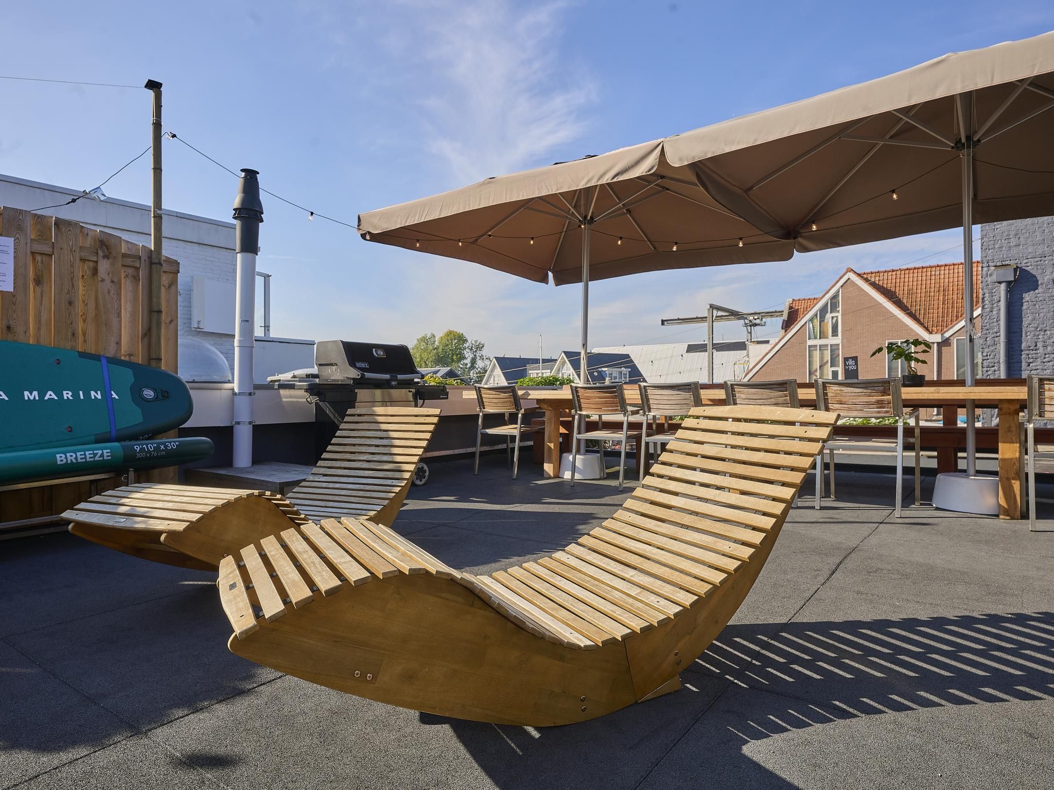 Outdoor lounge chairs under umbrellas, a barbecue grill, and a marina sign.