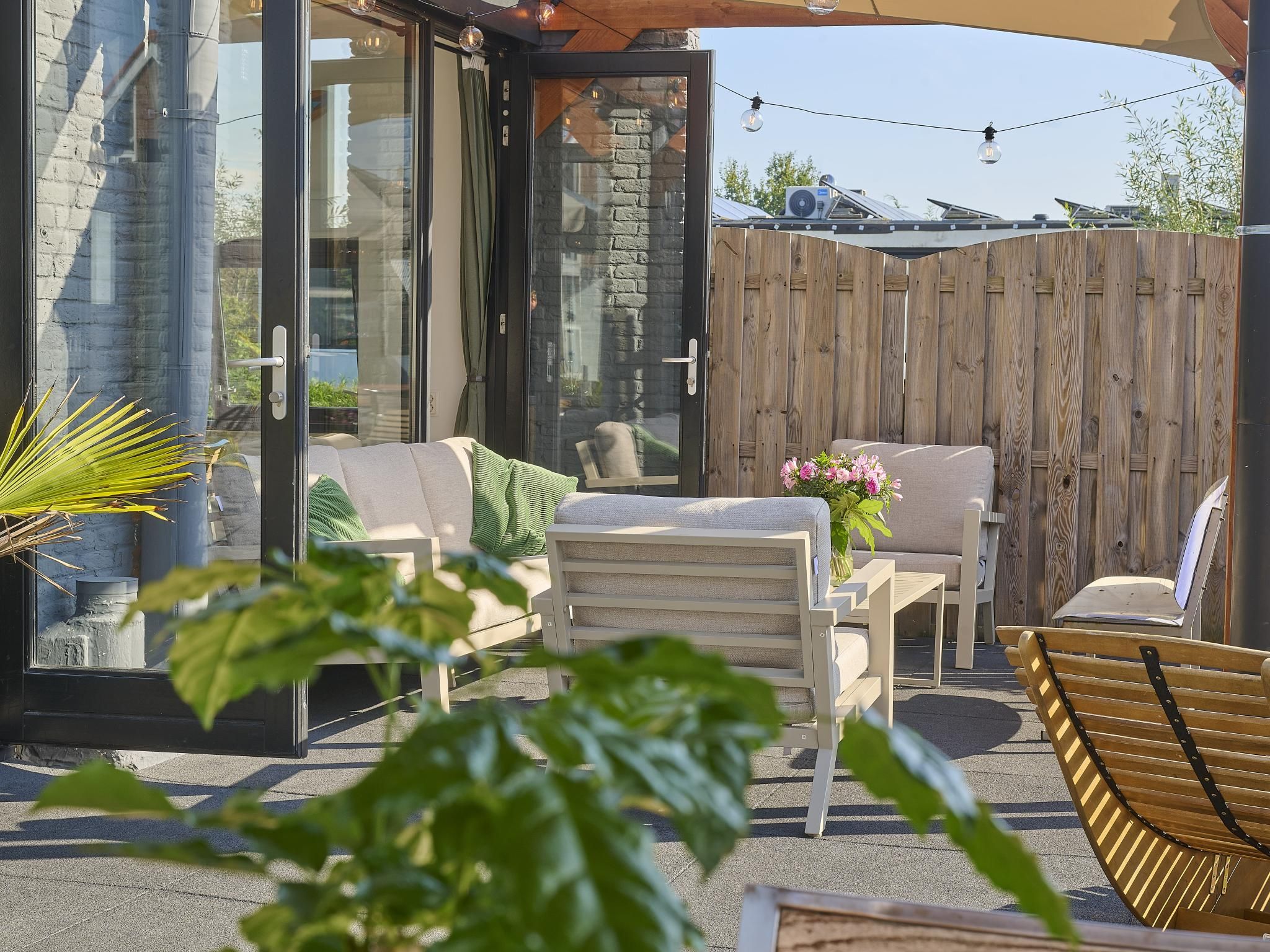 An outdoor patio with a glass door leading to a room, a wooden fence, and outdoor furniture.
