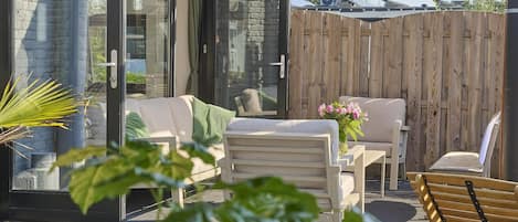 An outdoor patio with a glass door leading to a room, a wooden fence, and outdoor furniture.