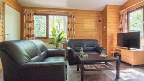 Een houten cabin interieur met twee leren banken, een salontafel, een televisie op een standaard en een raam met gordijnen.