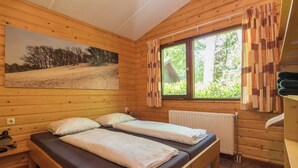 Een houten kamer met twee bedden, een raam met gordijnen, een radiator en een schilderij aan de muur.