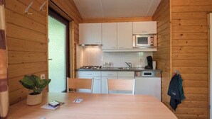 Een praktische keuken met witte kastjes, een magnetron en een gasfornuis. Er is een eettafel met stoelen, een potplant en een jas hangt aan de muur.