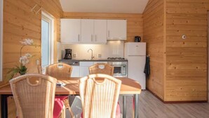 A compact kitchen with white cabinets, a microwave, and a refrigerator. There is a dining table with wicker chairs.