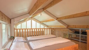 A room with a wooden ceiling, a bed with white linens, a window, and a shelf with folded items. - Romantic holiday home with sleeping loft for 2 (Heesch)