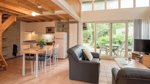 A spacious living area with a dining table, chairs, a sofa, a TV, and a balcony with a view of greenery. - Romantic holiday home with sleeping loft for 2 (Heesch)