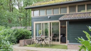 A two-story building with a patio area featuring a table and chairs, surrounded by greenery. - Romantic holiday home with sleeping loft for 2 (Heesch)