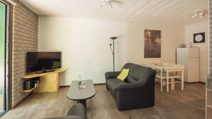A modern living room with a flat-screen TV, a sofa, a coffee table, and a dining area with a table and chairs. - Charming single-storey bungalow for 3. (Heesch)