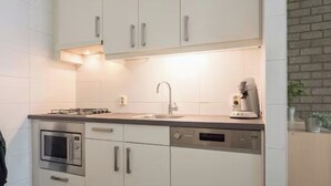 A modern kitchen with white cabinets, a built-in oven, a coffee machine, and a sink. - Charming single-storey bungalow for 3. (Heesch)