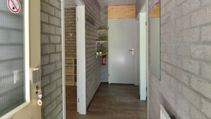 A narrow hallway with brick walls, a wooden floor, and a white door with a no smoking sign. - Charming single-storey bungalow for 3. (Heesch)