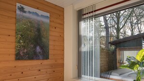 Un dormitorio con cabecera de madera, un ventanal con persianas, un radiador y una planta en maceta.