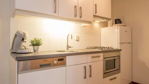 Una cocina compacta con armarios blancos, lavavajillas integrado, estufa y microondas.
