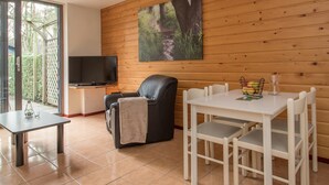 Una habitación acogedora con televisión, un sillón de cuero, una mesa de comedor con sillas y un cuadro de un sendero forestal.