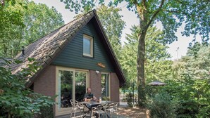 A small, rustic cabin with a brick exterior and a sloped roof, featuring a patio with outdoor seating and a large window. - Detached lodge with pond view for 4 (Heesch)