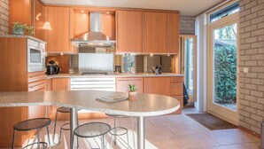 A modern kitchen with wooden cabinets, a stainless steel range hood, a built-in oven, and a large island with bar stools.
