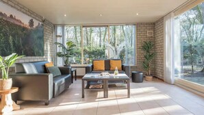 A spacious living room with a large window, a sofa, a coffee table, and several potted plants.