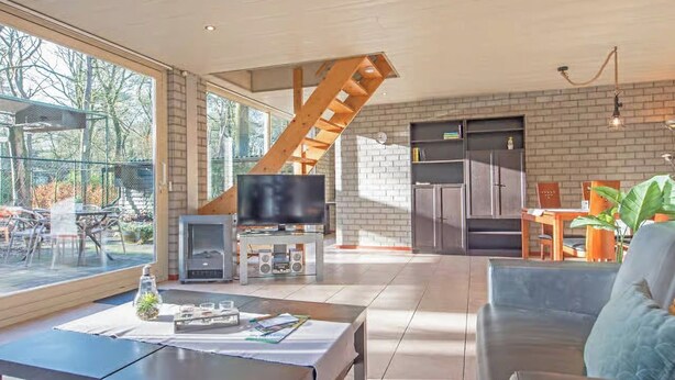 A modern interior with a large window, a staircase, a television, and a dining area.