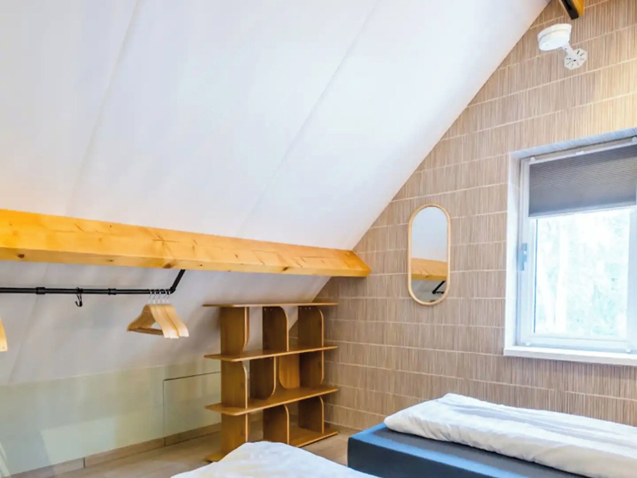 Een slaapkamer met een schuine plafond, een houten plank, een bed en een raam met uitzicht.
