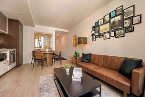 Ein modernes Wohnzimmer mit Ledersofa, einem Essbereich mit Stühlen, einer Küche mit Geräte und einer Wand mit gerahmten Bildern.