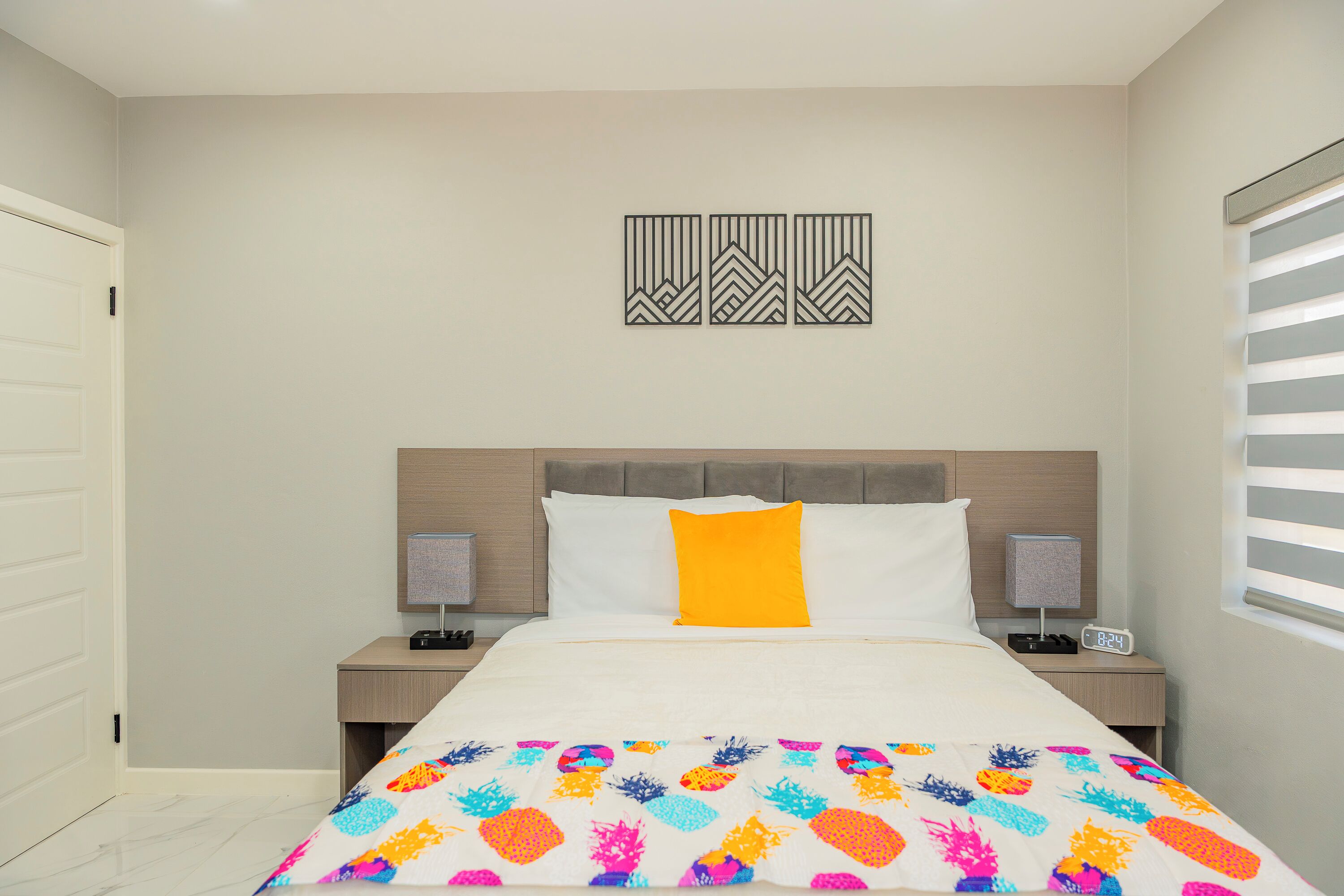 A bedroom with a bed, two bedside tables, a nightstand, a wall art piece, and a window with blinds.