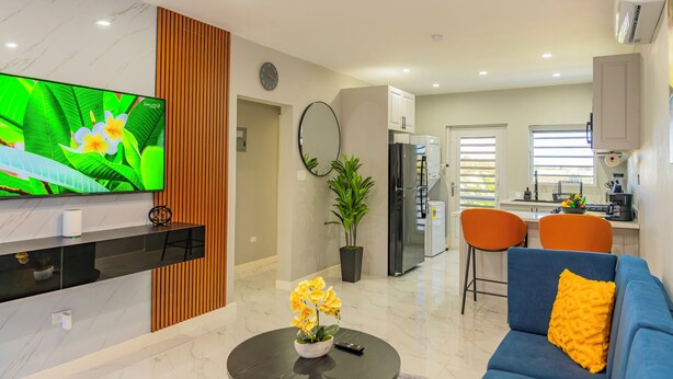 Una sala de estar moderna con televisor, sofá, mesa de centro y una zona de comedor con sillas.