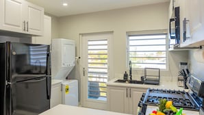 Una cocina moderna con armarios blancos, un refrigerador negro, una estufa y una ventana con persianas.