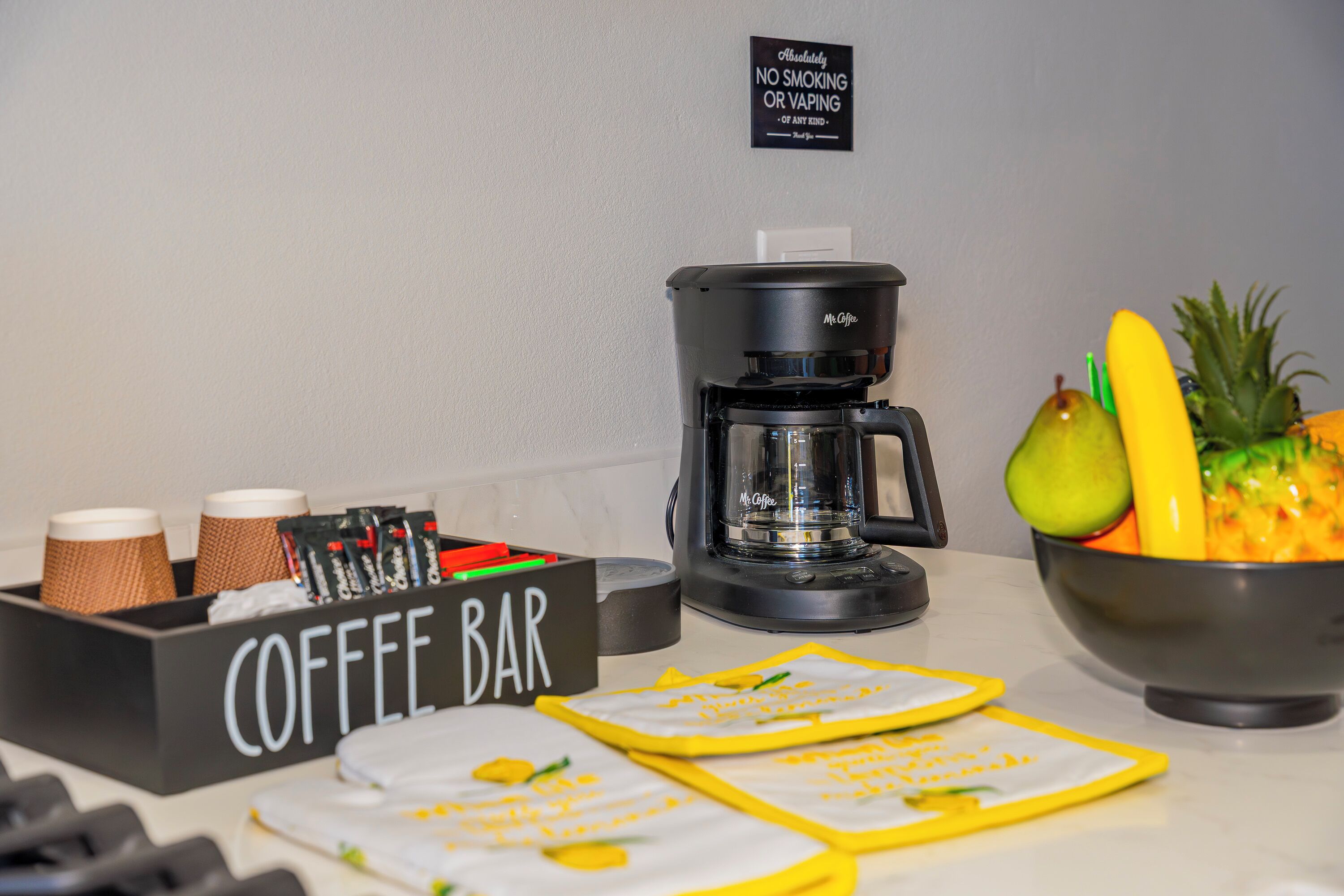 En kaffebar med en kaffemaskin, en skylt som förbjuder rökning och en skål med frukt.
