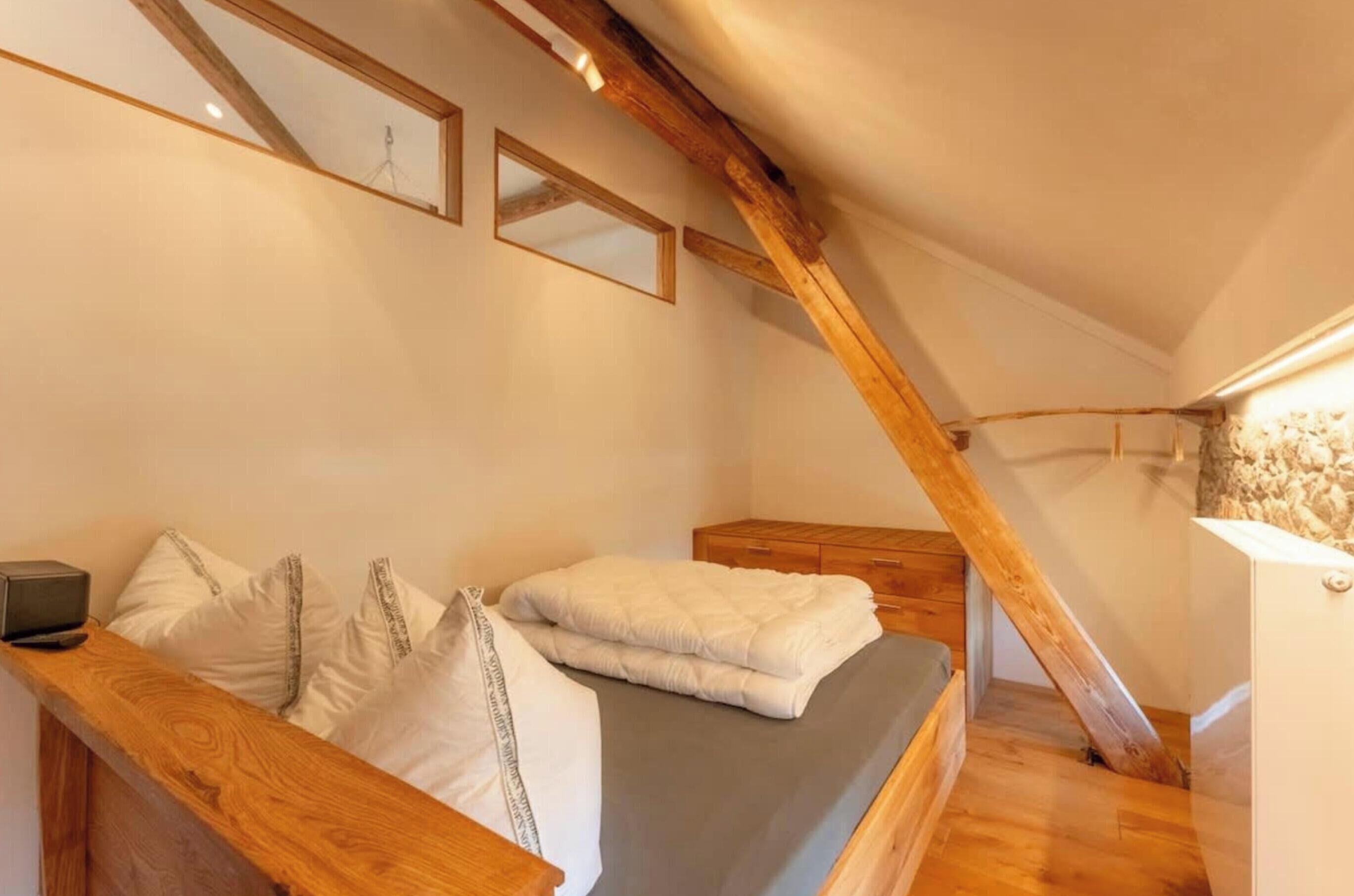 A bedroom with a wooden bed, a bedside table, a mirror, and a sloped ceiling with exposed beams.