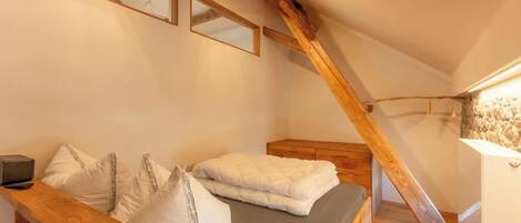 A bedroom with a wooden bed, a bedside table, a mirror, and a sloped ceiling with exposed beams.