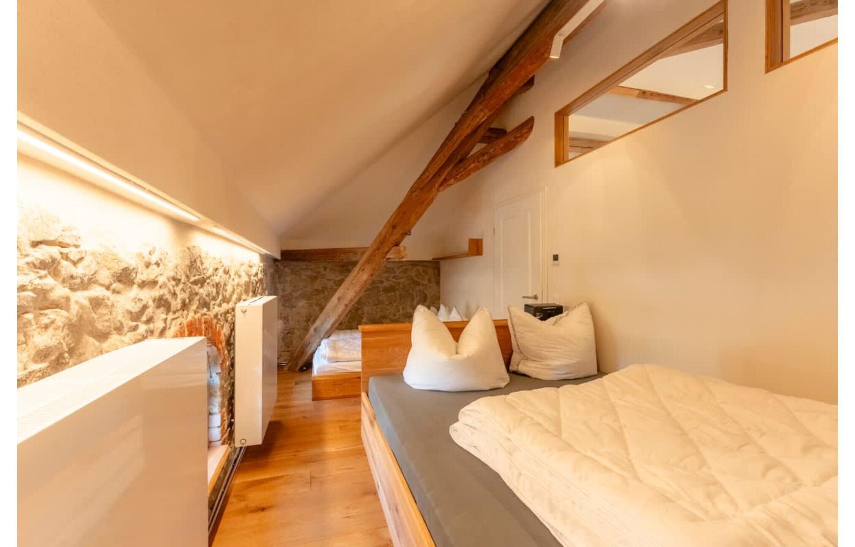 A bedroom with a stone wall, wooden beams, a bed, and a bedside table.