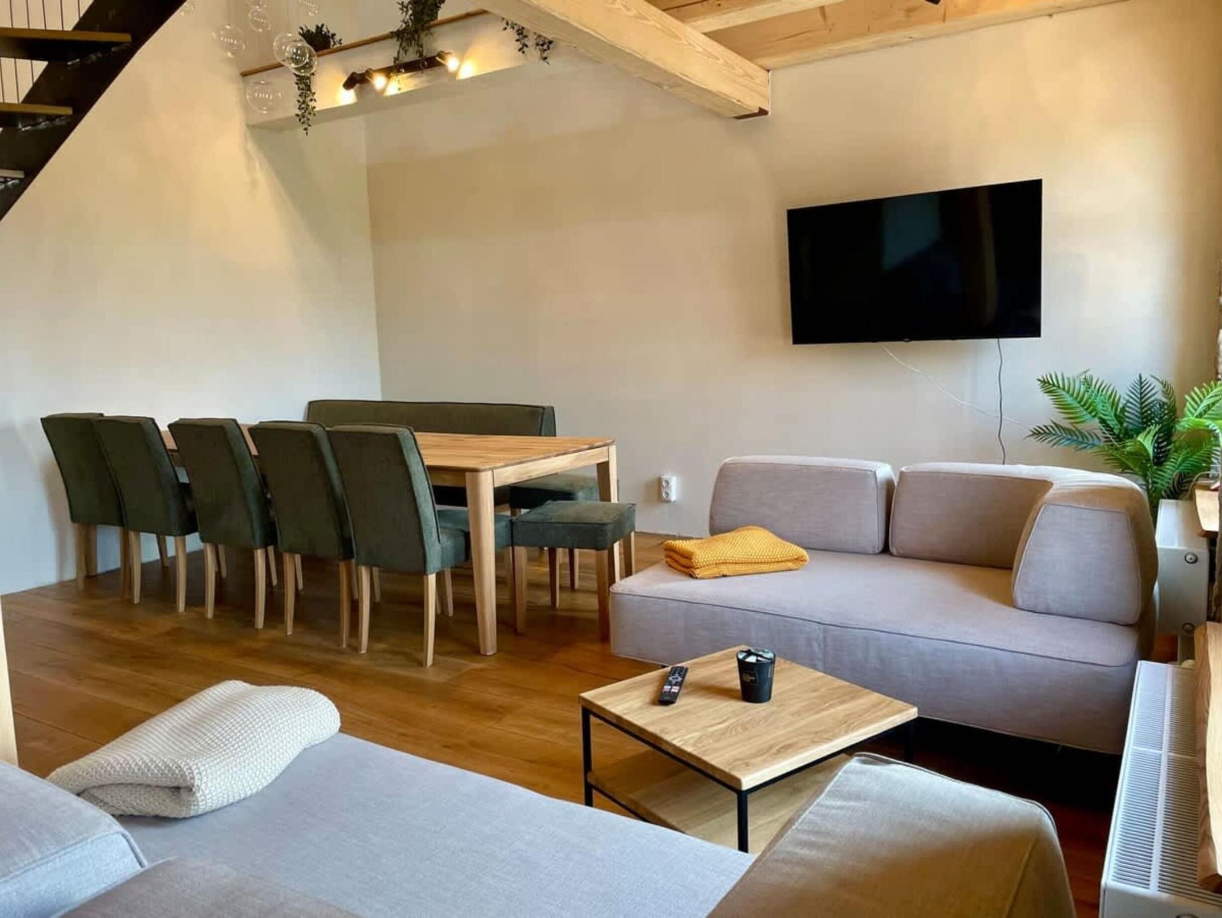 A modern living room with a sofa, a dining table with chairs, a TV mounted on the wall, and a small table with a remote control.