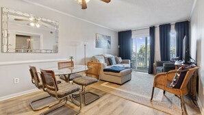 A modern living room with a glass dining table, wicker chairs, a sofa, and a ceiling fan. - Shore Drive Gem: Walk to Beach, Pool & Apache Pier (Myrtle Beach)