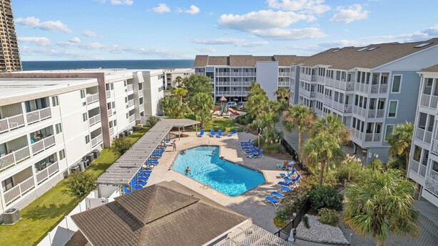 A hotel with a swimming pool surrounded by lounge chairs, palm trees, and a view of the ocean. - Shore Drive Gem: Walk to Beach, Pool & Apache Pier (Myrtle Beach)