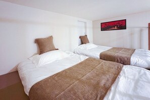 Habitación de hotel con dos camas, ropa de cama blanca, mantas marrones y un cuadro en la pared.