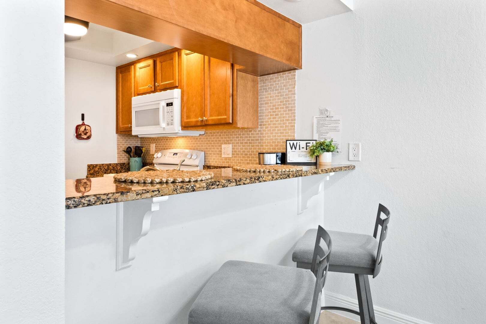 A kitchen with wooden cabinets, a microwave, a stove, granite countertops, and a bar stool.