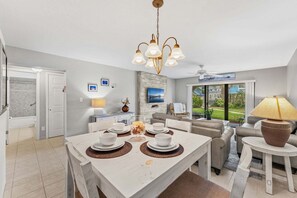 A modern kitchen with a dining area, a TV mounted on the wall, and a view of the outdoors.