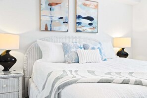 A neatly made bed with a white and gray patterned bedspread, two matching pillows, and a wicker headboard. There are two bedside tables with lamps, and the room has a clean, minimalist decor.